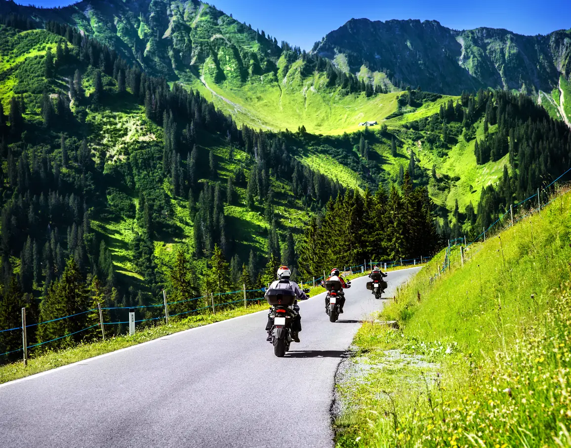 Tre motorsyklister på rad langs en svingete fjellvei