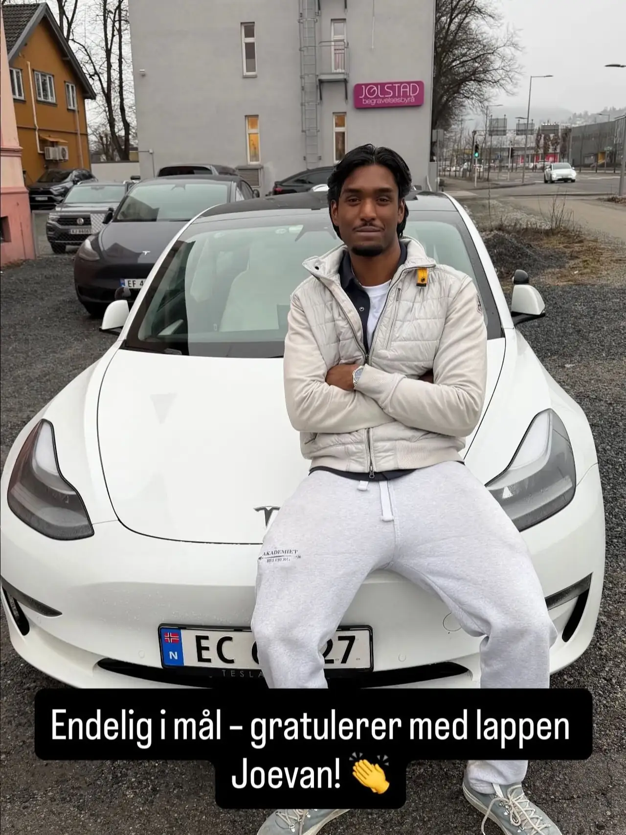 Elev sitter på panseret av skolens Tesla etter bestått prøve